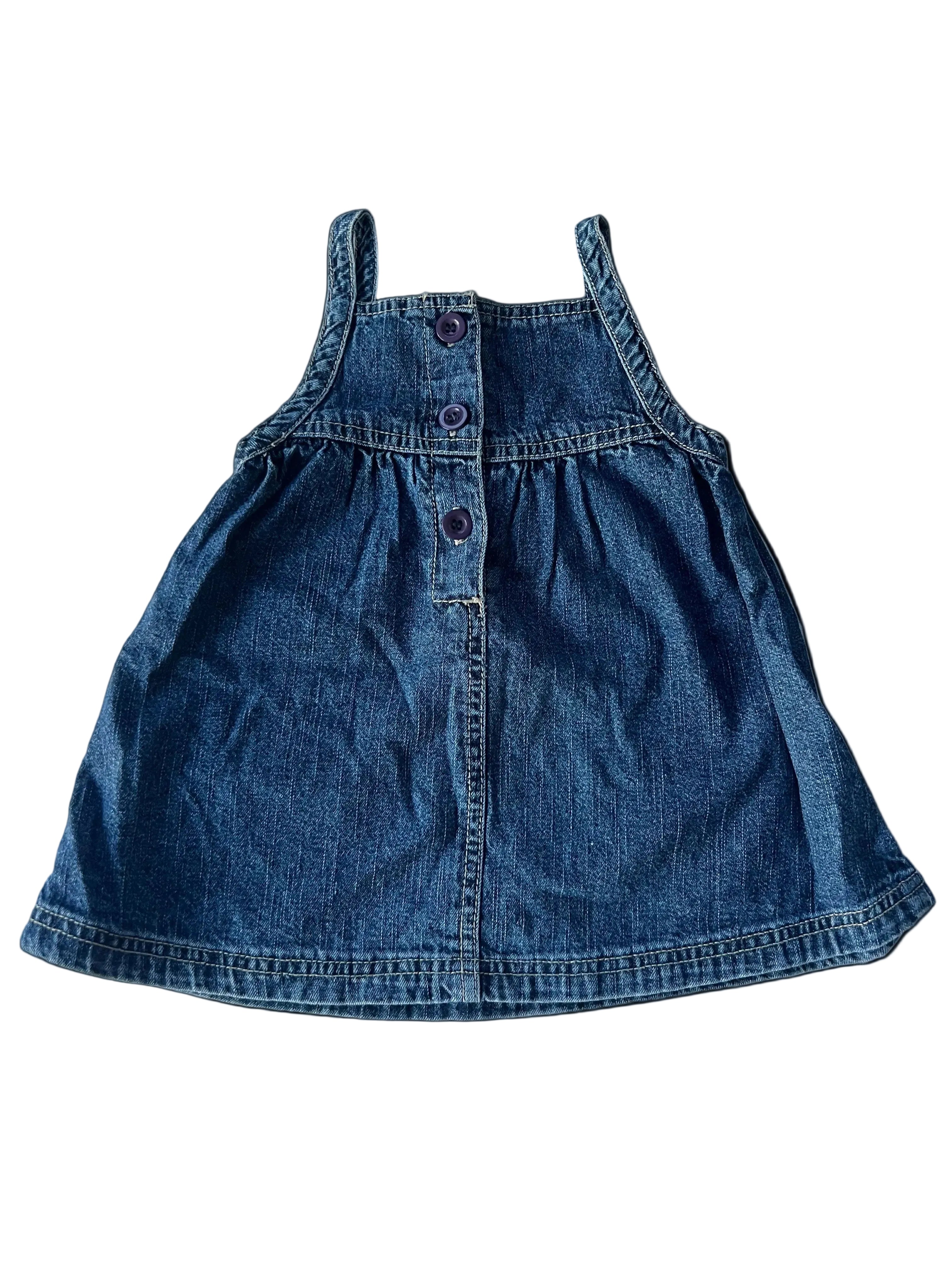 A small blue denim pinafore dress laid flat on a white fabric background.
